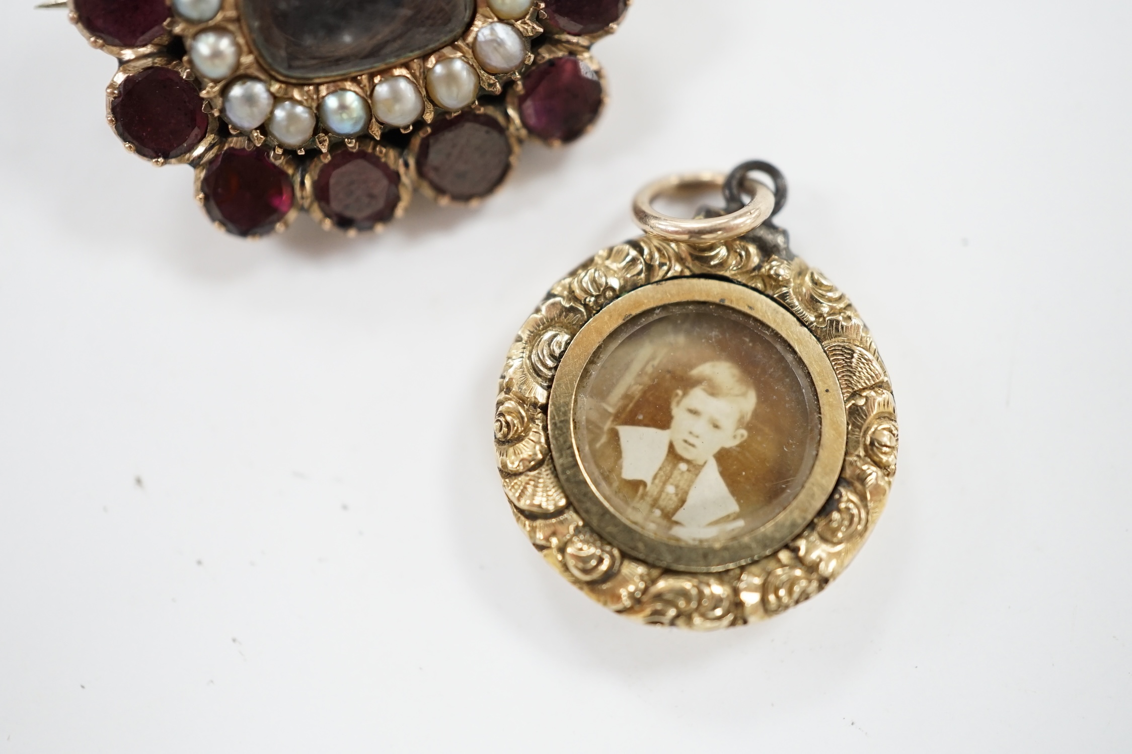 An early Victorian yellow metal, garnet and split pearl set mourning brooch, with engraved monogram, 23mm and a George IV mourning locket, inscribed 'Martha Lloyd, ob. 8th May, 1824 at 53'. Condition - fair